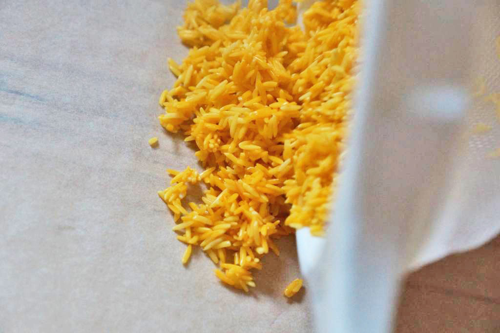 Reis aus einem Sieb auf Backpapier ausbreiten